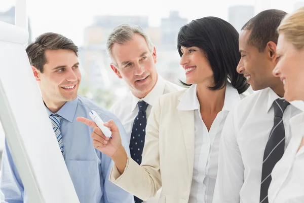 Colegas assistindo empresária feliz apontando para quadro branco — Fotografia de Stock