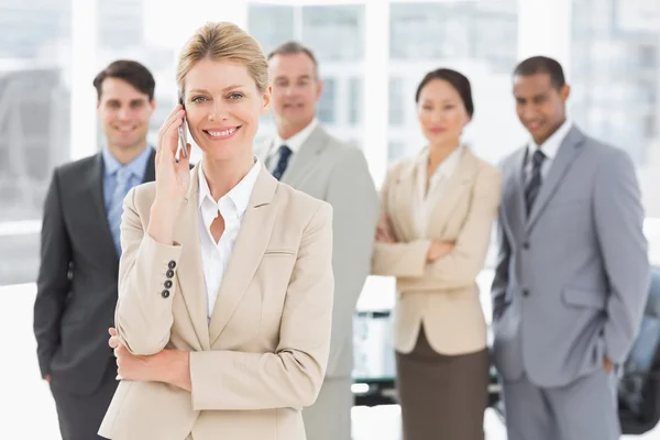 Businesswoman on the phone smiling at camera with team behind he — Stock Photo, Image