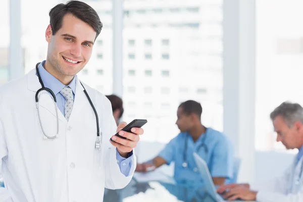 Doctor text messaging with group around table in hospital — Stock Photo, Image