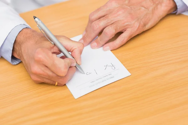 Läkare som sitter vid sitt skrivbord skrift på recept pad — Stockfoto