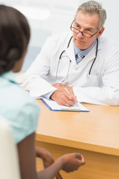 Vážné lékař poslouchá svého pacienta a psaní poznámek — Stock fotografie