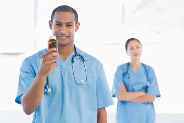 Smiling doctor holding a bottle of pills with colleague — Stock Photo, Image