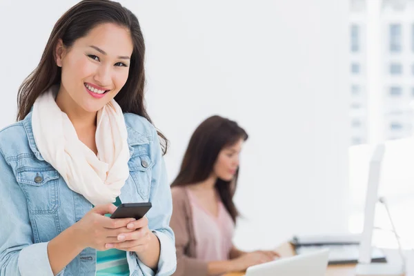 Smiling young woman text messaging in office — Stock Photo, Image