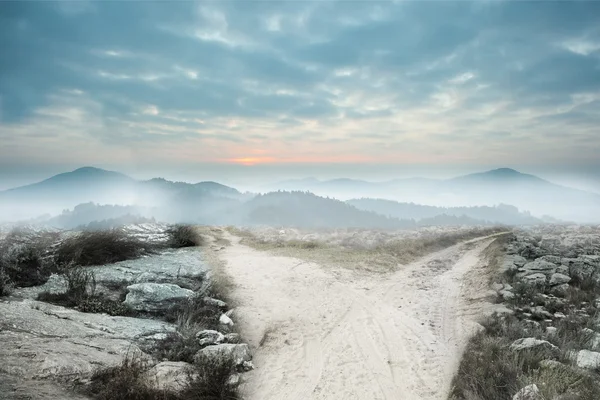 Dusty path leading to misty mountains — Stock Photo, Image