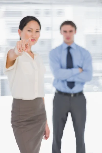 Businesswoman pointing towards camera with man in office — Stock Photo, Image