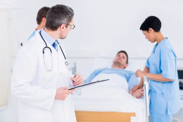 Arzt hält Berichte mit Patient und Chirurg im Hintergrund — Stockfoto