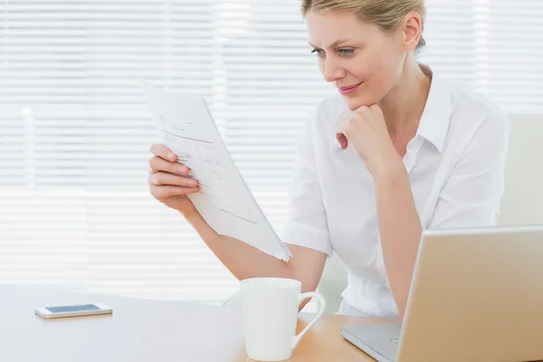 Geschäftsfrau liest neben Laptop am Schreibtisch ein Dokument — Stockfoto
