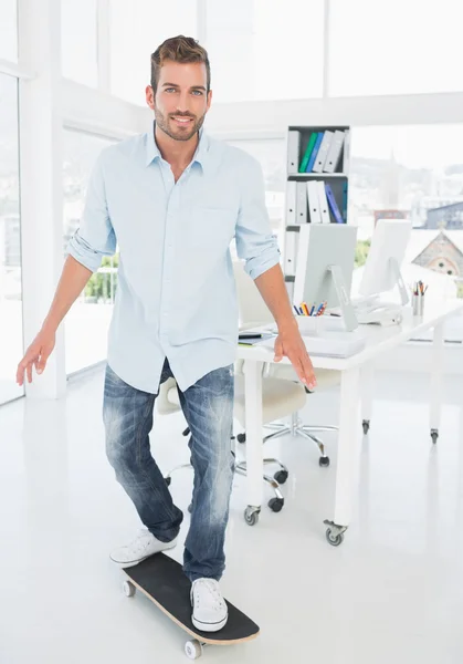 Happy young man skateboarding in creative office — Stock Photo, Image