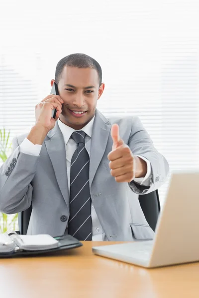 Empresário sorridente gesticulando polegares para cima enquanto de plantão — Fotografia de Stock