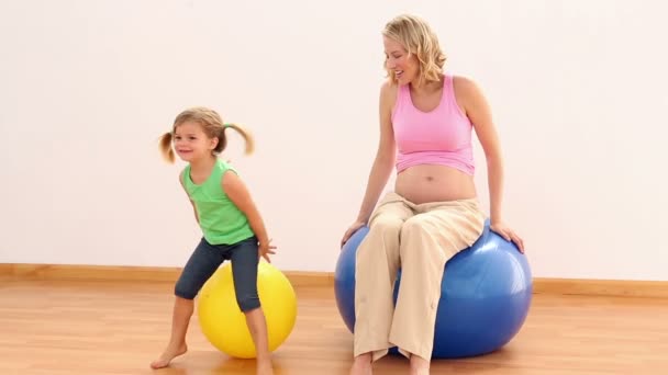 Mulher grávida sentada na bola de exercício com sua menina — Vídeo de Stock