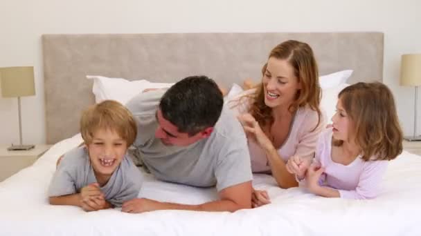 Lindos padres e hijos acostados en la cama bromeando y cosquillas entre sí — Vídeo de stock