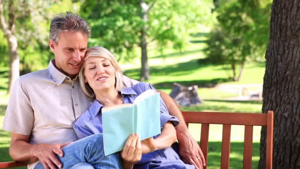 Pareja cariñosa sentada en el banco del parque leyendo — Vídeos de Stock