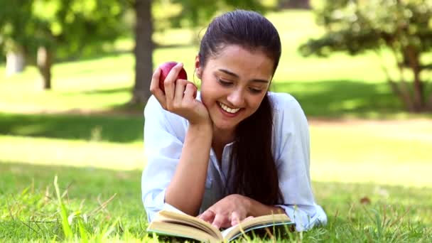 Hübsches Mädchen, das im Gras liegt und ein Buch liest — Stockvideo