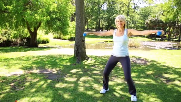 Femme blonde soulevant des haltères dans le parc — Video