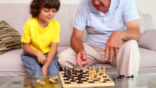 Старший чоловік сидить на дивані зі своїм онуком граючи в шахи — стокове відео