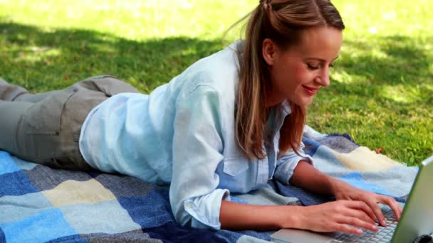 Bionda usando il suo computer portatile sdraiato su una coperta nel parco — Video Stock