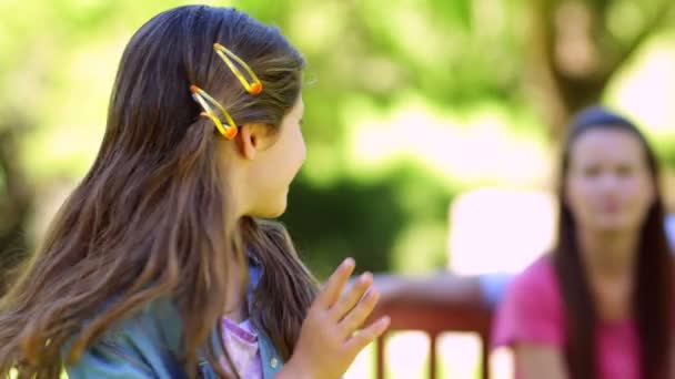 Девушка машет с семьей на скамейке в парке — стоковое видео