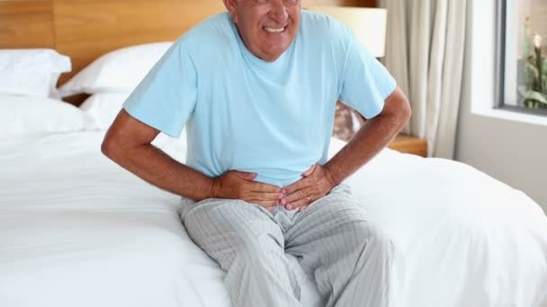 Hombre mayor sentado en la cama con dolor de estómago — Vídeo de stock