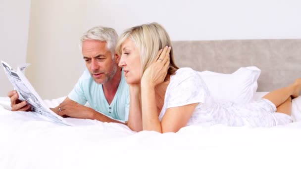 Pareja acostada en la cama leyendo el periódico juntos — Vídeos de Stock