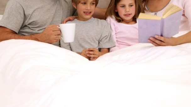 Χαμογελώντας γονείς και παιδιά διαβάζοντας μαζί στο κρεβάτι — Αρχείο Βίντεο