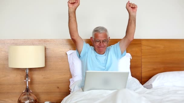 Senior man sitting in bed using laptop and cheering — Stock Video