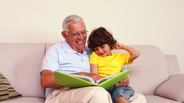 Hombre mayor sentado en el sofá con su nieto mirando álbum de fotos — Vídeos de Stock