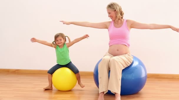 Ξανθιά έγκυος γυναίκα που κάθεται στο μπάλα γυμναστικής με κοριτσάκι — Αρχείο Βίντεο