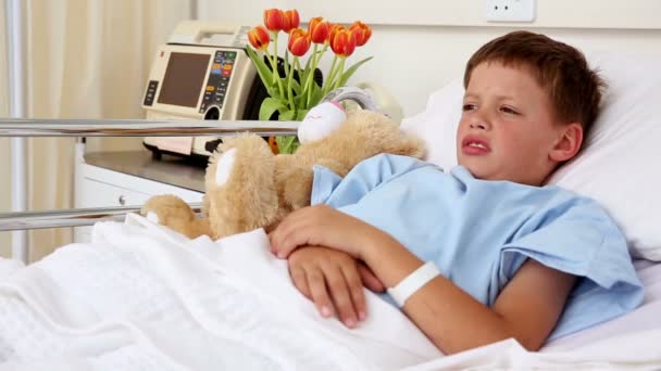 Маленький больной мальчик лежит в постели с плюшевым мишкой — стоковое видео