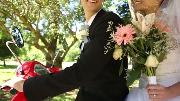 Šťastní novomanželé jezdecké červený skútr v parku — Stock video