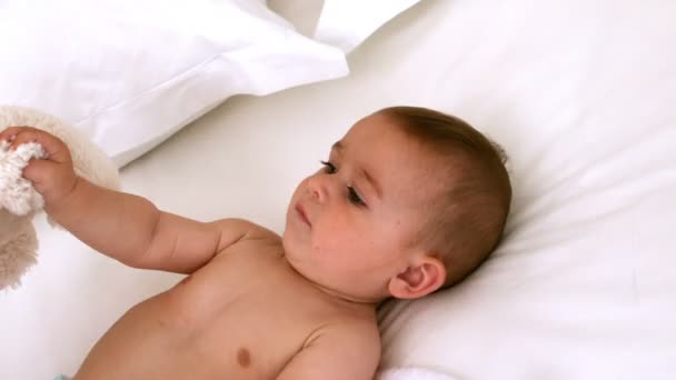 Lindo bebé en una cama con oso de peluche — Vídeo de stock