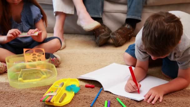 Siblings doing arts and crafts on the rug while parents watch — Stock Video