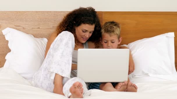 Mother and son using laptop lying on bed — Stock Video