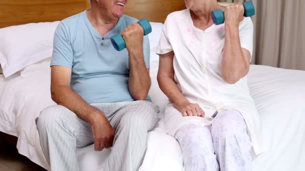 Senior couple sitting on bed lifting dumbbells — Stock Video