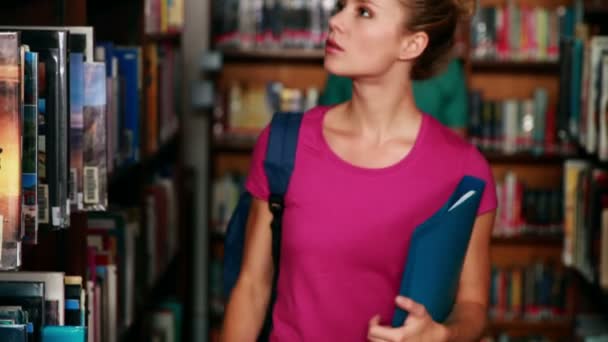 Pretty student picking out a book in the library — Stock Video