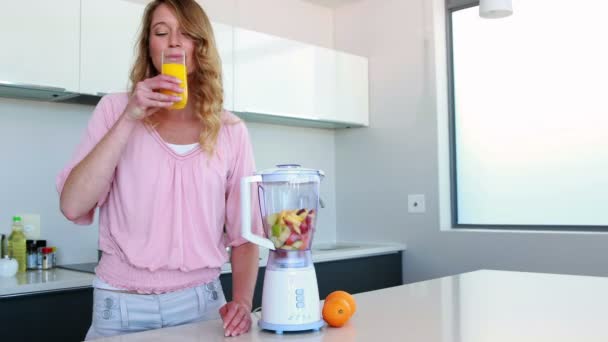 Mulher na cozinha bebendo suco de laranja ao lado do espremedor — Vídeo de Stock