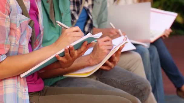 Studenten zitten in een rij schrijven in notitieboekjes — Stockvideo