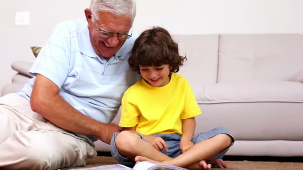 Uomo anziano seduto sul pavimento con suo nipote guardando album fotografico — Video Stock