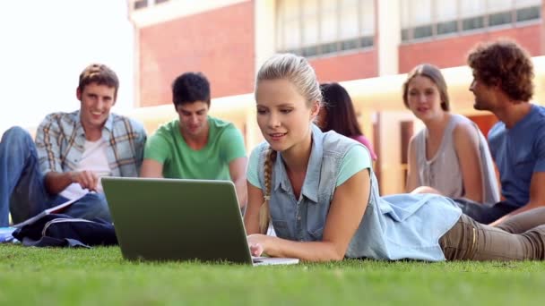 Studente biondo utilizzando laptop con compagni di classe seduti dietro sull'erba — Video Stock