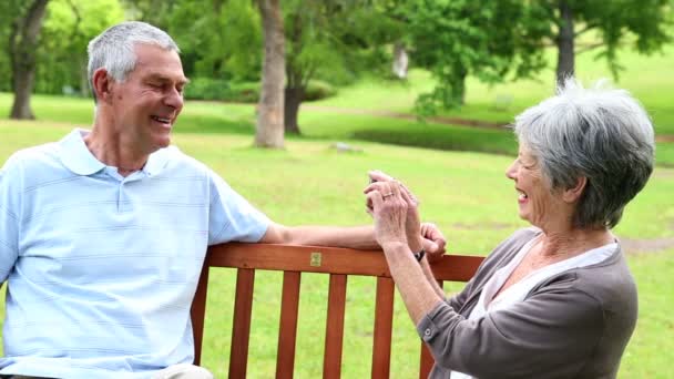 Casal aposentado sentado em um banco de parque tirando uma foto — Vídeo de Stock