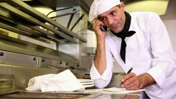 Chef guapo escribiendo en el portapapeles mientras habla por teléfono — Vídeos de Stock