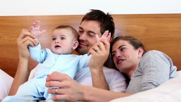 Gelukkige ouders liggend op bed met baby zoon — Stockvideo