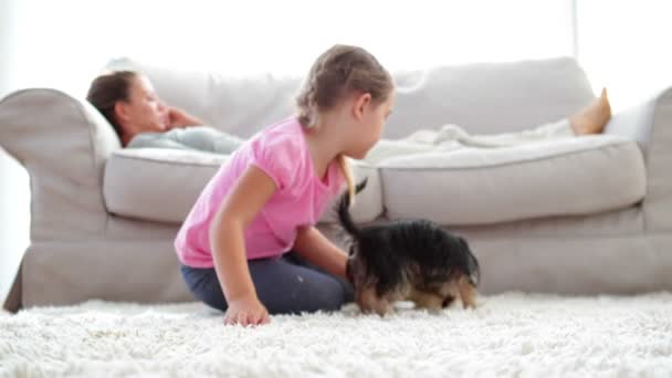 Mädchen spielt mit Hund und Knochen und ihre Mutter liest auf dem Sofa — Stockvideo