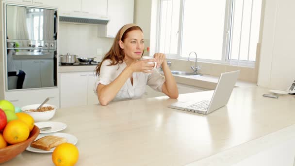 Brunette drinking coffee and thinking in front of laptop — Stock Video