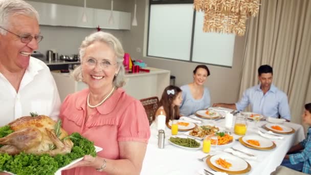 Stolta morföräldrar håller stekt kyckling med familj bakom dem. — Stockvideo