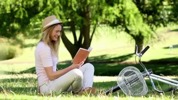 Pretty girl reading beside her bike in the park — Stock Video