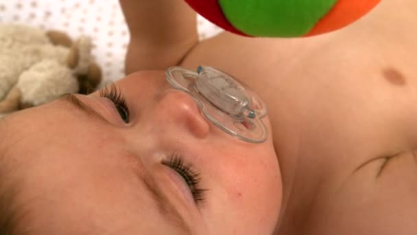 Дитина лежить в дитячому ліжечку тримає іграшку — стокове відео