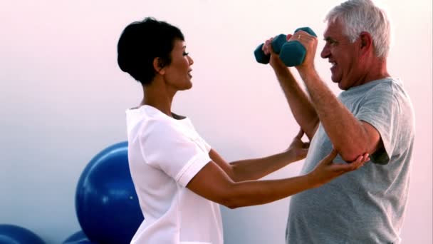 Äldre man lyfta hand vikter med sjukgymnast — Stockvideo