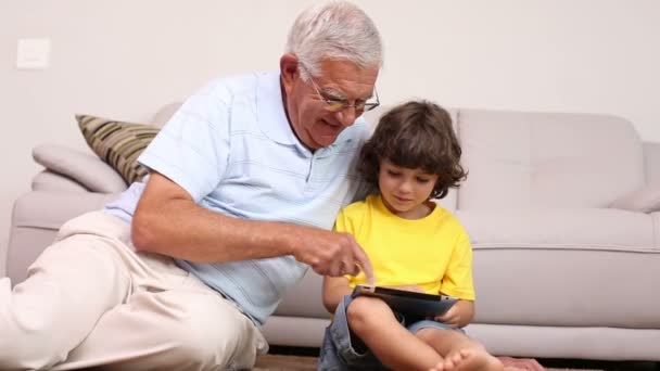 Hombre mayor sentado en el suelo con su nieto usando tableta — Vídeos de Stock