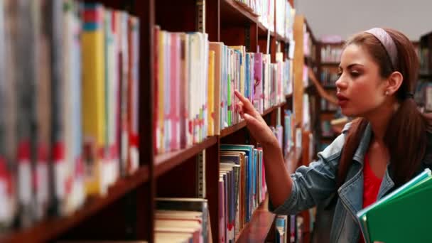 Estudiante sonriente escogiendo un libro de texto en la biblioteca — Vídeos de Stock