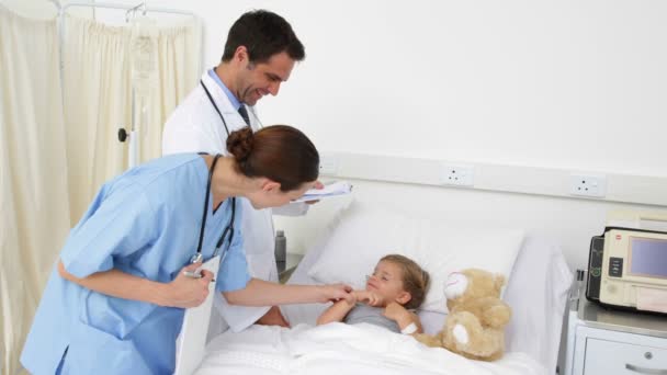 Sick little girl lying in bed talking to nurse and doctor — Stock Video